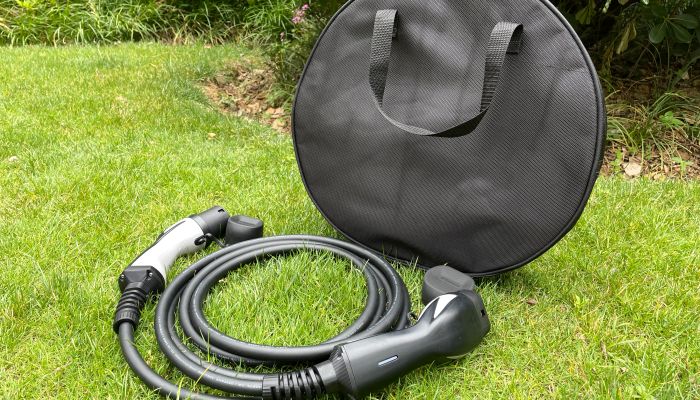 Cabo de carregamento Wissenergy EV enrolado cuidadosamente na grama ao lado de uma bolsa de transporte preta redonda com alças.
