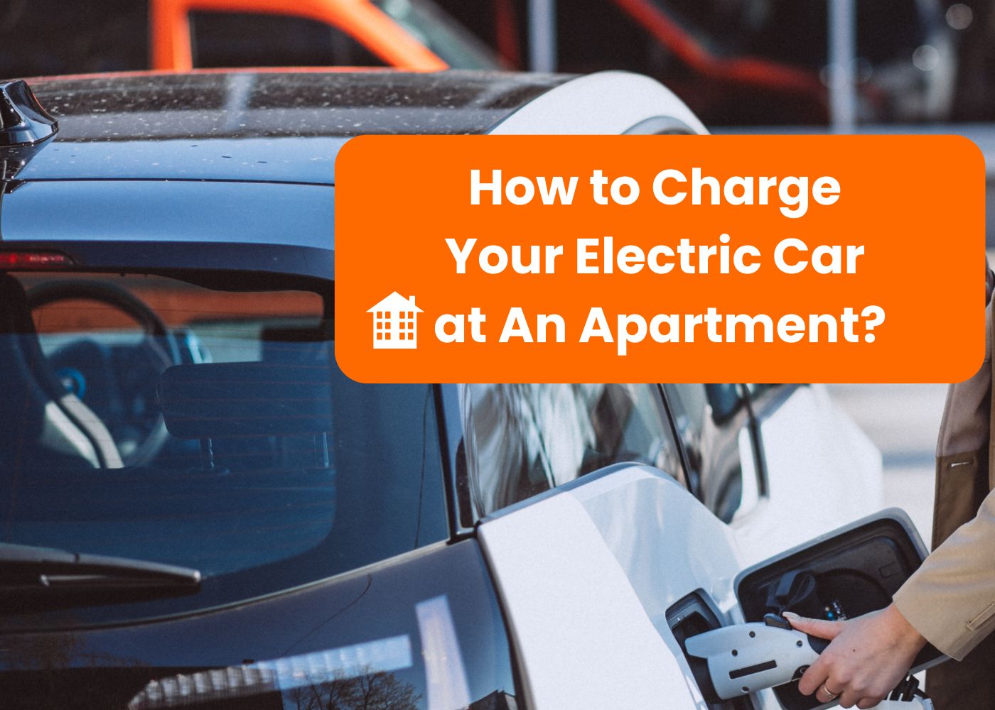 A person is charging an electric car at an apartment complex. The image shows the charging cable being plugged into the car with a clear view of the car's rear and the charging station. The text on the image asks how to charge an electric car in an apartment, highlighting the challenge of finding charging options in such living situations.