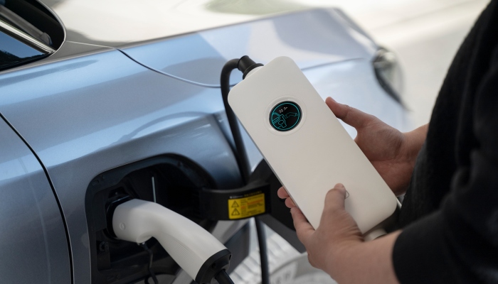 Person holding a Wissenergy SQP039 220V portable EV charger while it charges an electric vehicle, with charging status visible on the display.