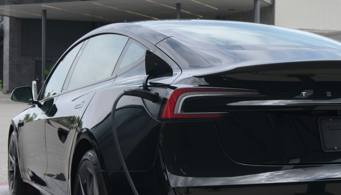 Black Tesla electric car connected to a charging cable at a charging station.