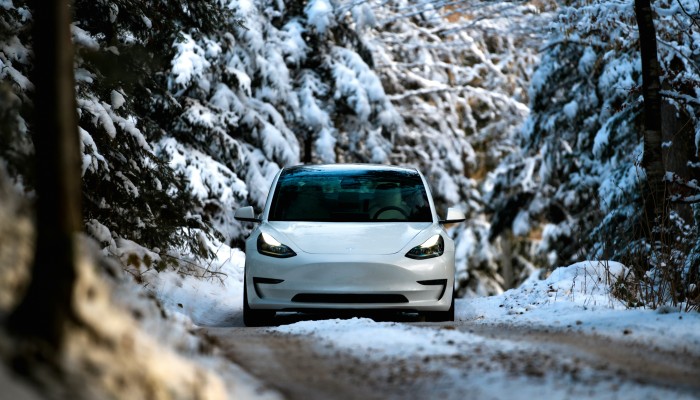 White Tesla Model 3 charging outdoors on a snowy day, parked beside a path surrounded by light snow and greenery.